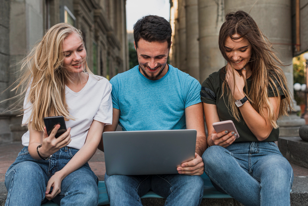 Group of young adults using laptop and phones outdoors, guided by a skilled reputation management expert