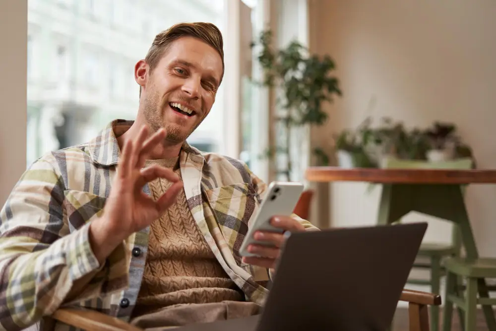 Smiling man giving OK sign while holding phone and laptop, Are We Dating the Same Guy