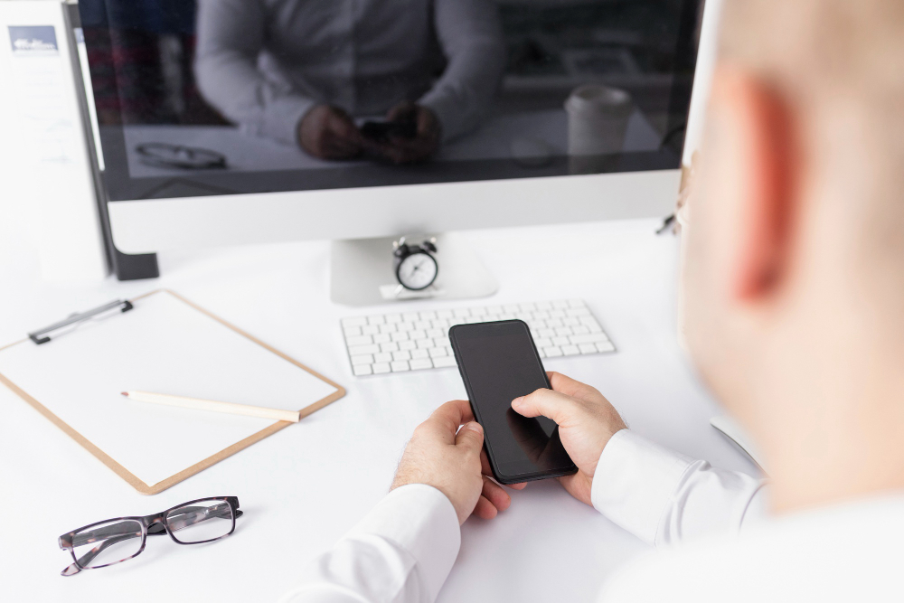 Businessman holding smartphone at desk during employer review cleanup tasks