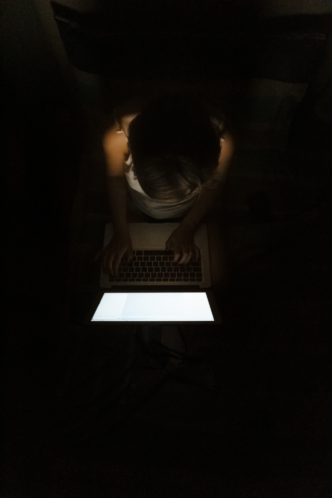 Person typing on a glowing laptop screen in a dark room, engaged in dark web monitoring tasks.