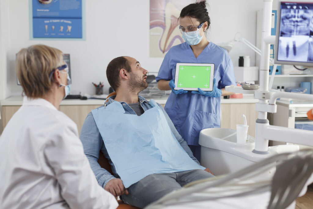 dentist woman holding mock up green screen chroma key tablet with isolated display discussing oral hygiene with man patient stomatological consultation dental office stom